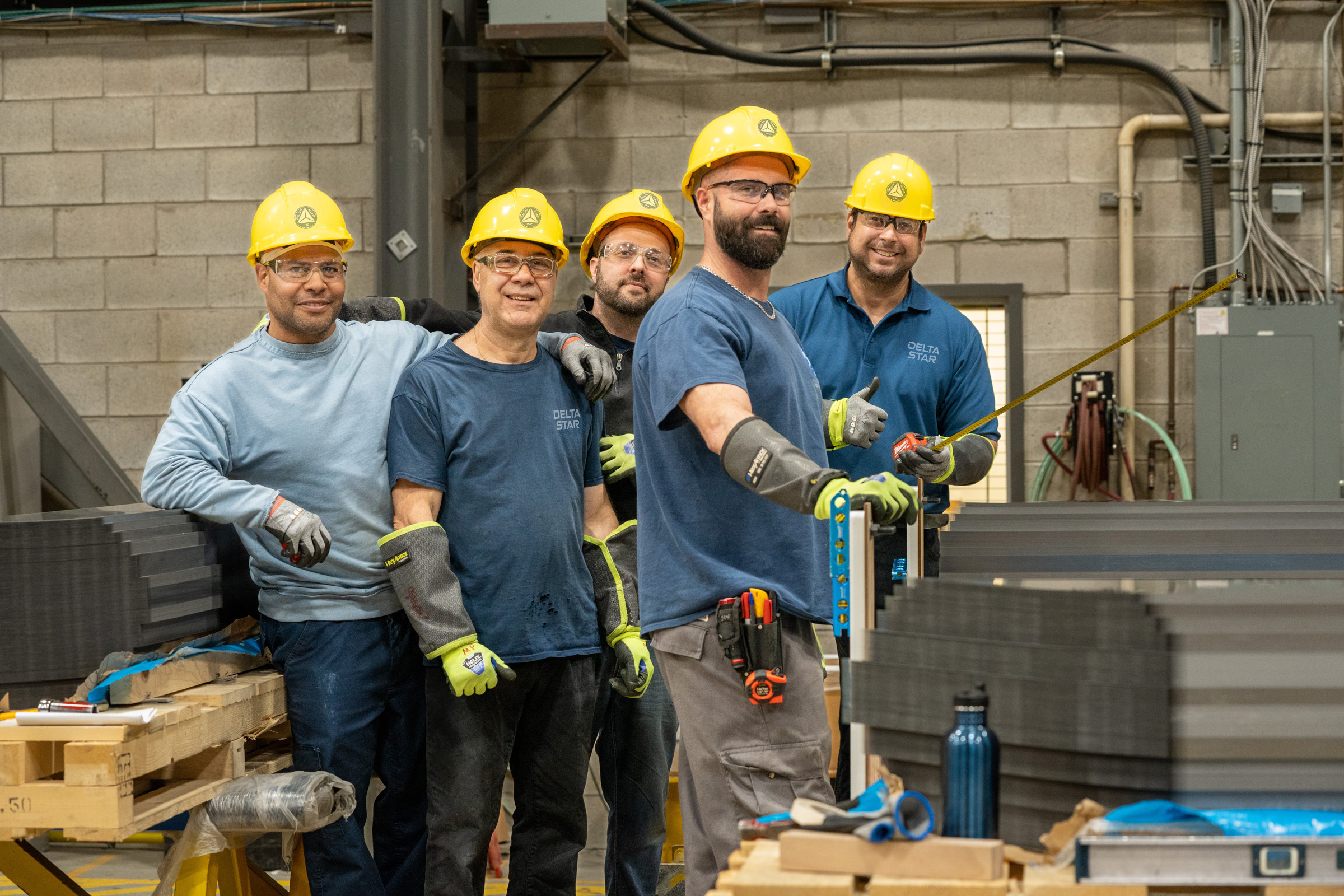 A group of manufacturing employees wearing safety helmets pose together on the production floor.