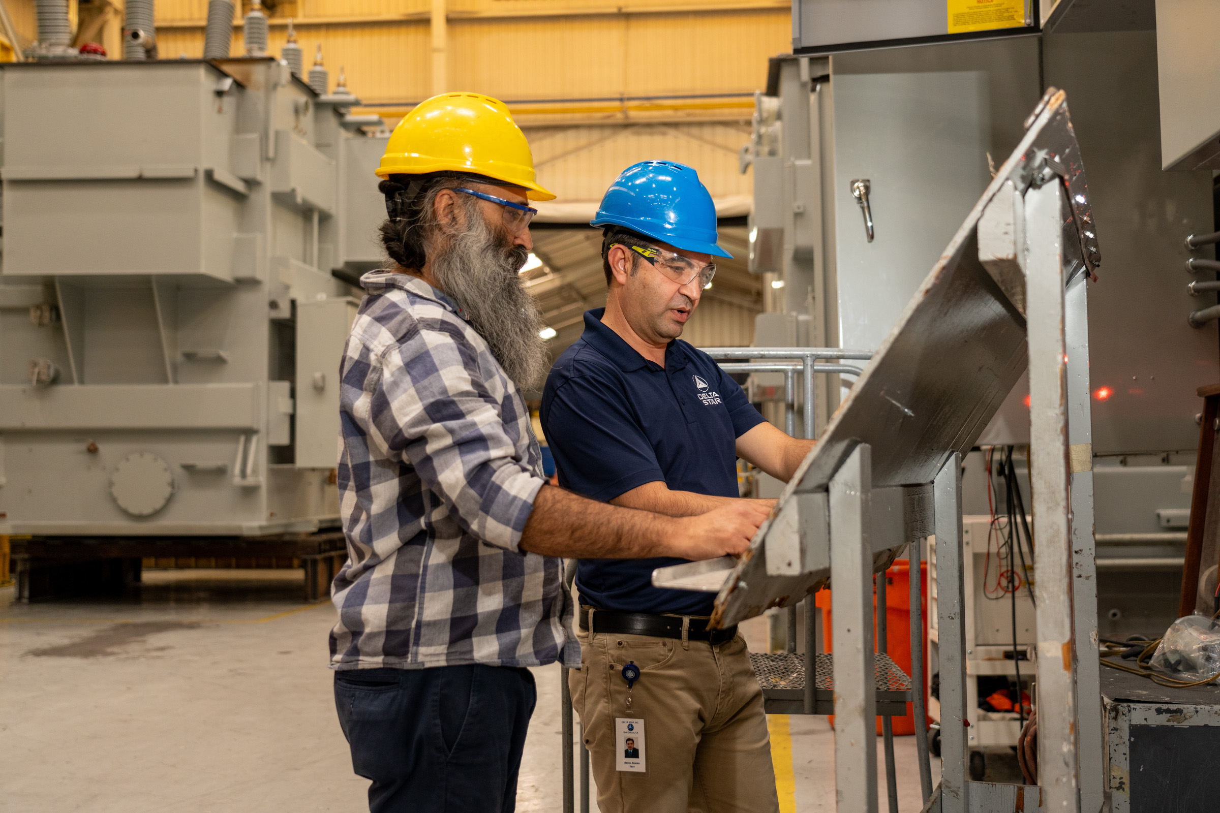 Two employees wearing safety helmets review technical documents inside a manufacturing facility.