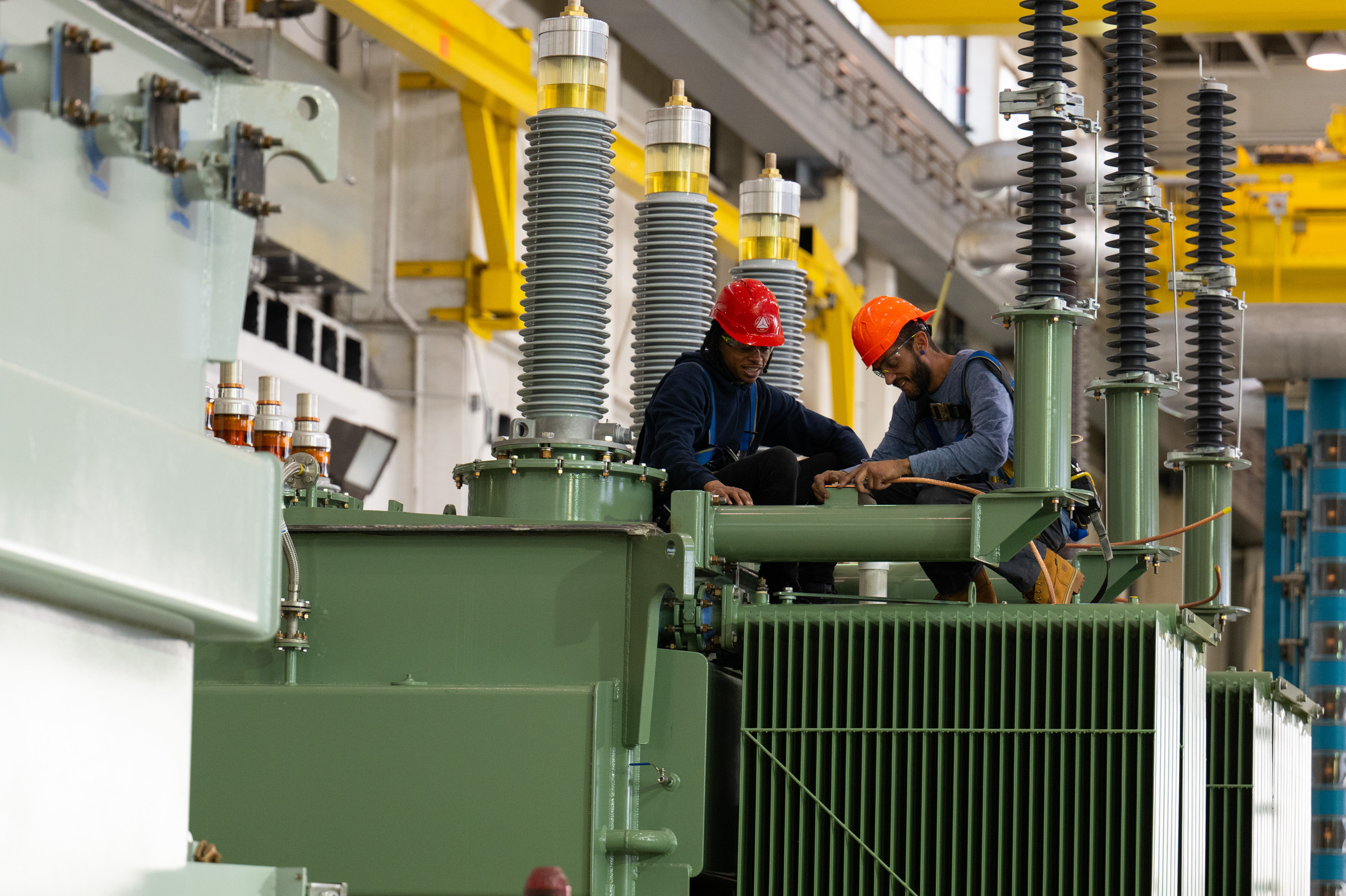 Technicians assembling a power transformer inside an industrial facility.